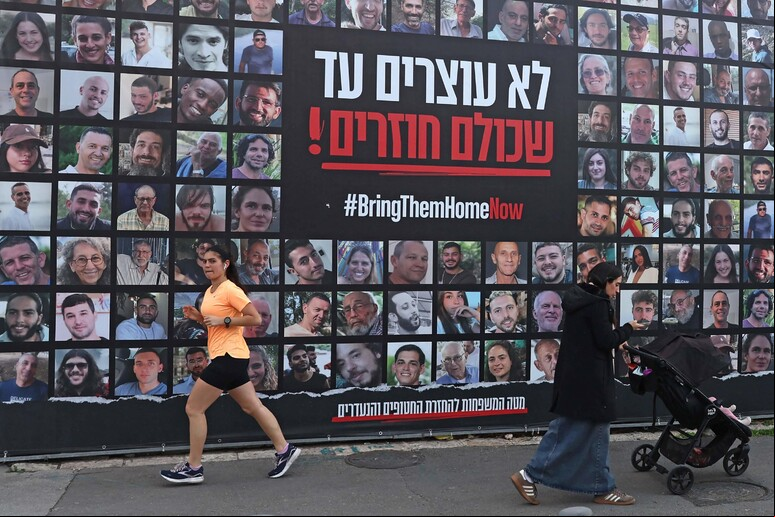 Pessoas ando por um outdoor com retratos dos reféns mantidos na Faixa de Gaza © ANSA/AFP